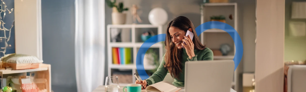 Remote worker on a phone call, taking notes at a laptop in a bright home office